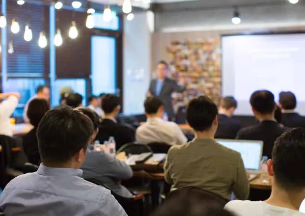 a group of people sitting at tables in front of a screen
